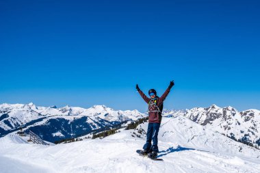 10 Mart 2019. Saalbach, Avusturya. Kar kayakçısı kar kaplı bir yamaçta kayıyor arkasında mavi gökyüzüne karşı kar tozu bırakıyor.