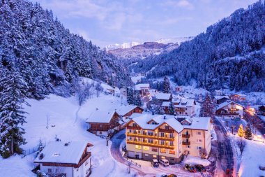 Beautiful panoramic view of Dolomites mountains at dusk during winter time. Magical winter mountain purple sunset with a mountain ski resort village. Christmas time.