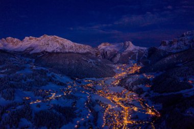 Beautiful panoramic view of Dolomites mountains at dusk during winter time. Magical winter mountain purple sunset with a mountain ski resort village. Christmas time.