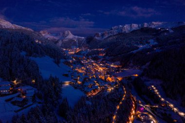 Beautiful panoramic view of Dolomites mountains at dusk during winter time. Magical winter mountain purple sunset with a mountain ski resort village. Christmas time.