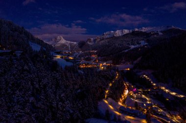 Beautiful panoramic view of Dolomites mountains at dusk during winter time. Magical winter mountain purple sunset with a mountain ski resort village. Christmas time.