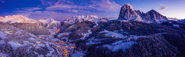 Beautiful panoramic view of Dolomites mountains at dusk during winter time. Magical winter mountain purple sunset with a mountain ski resort village. Christmas time.