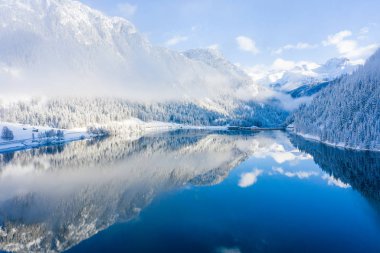 Magical Switzerland winter lake in the middle of the Alps surrounded by the magical forest covered in snow.