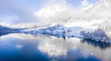 Magical Switzerland winter lake in the middle of the Alps surrounded by the magical forest covered in snow. 