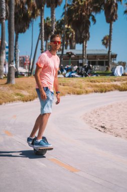 Venice sahilindeki bisiklet yolunda Los Angeles, Kaliforniya 'daki Pasifik Okyanusu' na doğru tek tekerlekli bir elektrikli bisiklet süren genç adam. Güzel yaz ruhu titreşimleri.