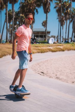 Venice sahilindeki bisiklet yolunda Los Angeles, Kaliforniya 'daki Pasifik Okyanusu' na doğru tek tekerlekli bir elektrikli bisiklet süren genç adam. Güzel yaz ruhu titreşimleri.