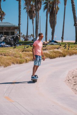 Venice sahilindeki bisiklet yolunda Los Angeles, Kaliforniya 'daki Pasifik Okyanusu' na doğru tek tekerlekli bir elektrikli bisiklet süren genç adam. Güzel yaz ruhu titreşimleri.