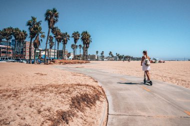 Venice plaj bisiklet şeridinde elektrikli scooter süren güzel bir kız. Plaj boyunca ve Pasifik Okyanusu boyunca. Kaliforniya 'nın Los Angeles' taki manzarası inanılmaz. Elektrikli scooter biçimi.