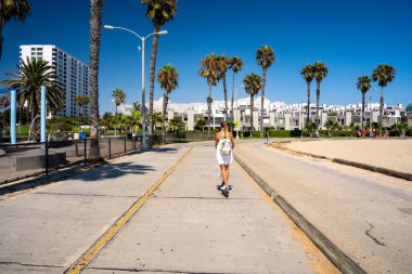 Venice plaj bisiklet şeridinde elektrikli scooter süren güzel bir kız. Plaj boyunca ve Pasifik Okyanusu boyunca. Kaliforniya 'nın Los Angeles' taki manzarası inanılmaz. Elektrikli scooter biçimi.