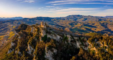 Monte Titano 'daki Guaita kalesinin hava manzaralı güzel manzarası ve arka planda San Marino şehri gün doğumunda. San Marino 'nun güzel tarihi merkezi. Tepenin tepesinde bir kale.