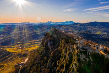 Monte Titano 'daki Guaita kalesinin hava manzaralı güzel manzarası ve arka planda San Marino şehri gün doğumunda. San Marino 'nun güzel tarihi merkezi. Tepenin tepesinde bir kale.
