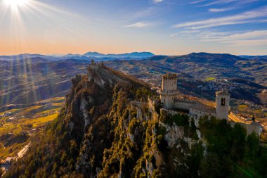 Monte Titano 'daki Guaita kalesinin hava manzaralı güzel manzarası ve arka planda San Marino şehri gün doğumunda. San Marino 'nun güzel tarihi merkezi. Tepenin tepesinde bir kale.