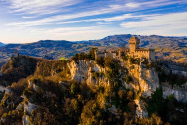 Monte Titano 'daki Guaita kalesinin hava manzaralı güzel manzarası ve arka planda San Marino şehri gün doğumunda. San Marino 'nun güzel tarihi merkezi. Tepenin tepesinde bir kale.