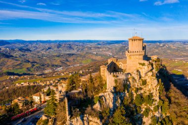 Monte Titano 'daki Guaita kalesinin hava manzaralı güzel manzarası ve arka planda San Marino şehri gün doğumunda. San Marino 'nun güzel tarihi merkezi. Tepenin tepesinde bir kale.