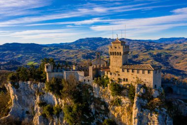 Monte Titano 'daki Guaita kalesinin hava manzaralı güzel manzarası ve arka planda San Marino şehri gün doğumunda. San Marino 'nun güzel tarihi merkezi. Tepenin tepesinde bir kale.