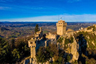Monte Titano 'daki Guaita kalesinin hava manzaralı güzel manzarası ve arka planda San Marino şehri gün doğumunda. San Marino 'nun güzel tarihi merkezi. Tepenin tepesinde bir kale.