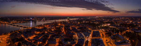 Панорамный воздушный вид на старый город Риги в сумерках во время волшебного розового заката. Город освещают уличные фонари.