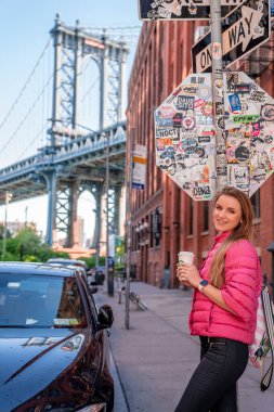 New York, ABD. 10 Mayıs 2019. Washington caddesinde kahve içen bir kız, Brooklyn 'de, arkasında Manhattan köprüsü olan..