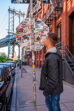 New York, ABD. 10 Mayıs 2019. Washington caddesinde yürüyen genç adam, Brooklyn 'de arka planda bir Manhattan köprüsü ile.
