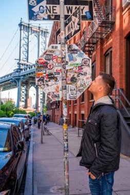 New York, ABD. 10 Mayıs 2019. Washington caddesinde yürüyen genç adam, Brooklyn 'de arka planda bir Manhattan köprüsü ile.