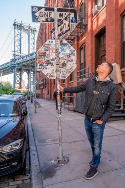 New York, ABD. 10 Mayıs 2019. Washington caddesinde yürüyen genç adam, Brooklyn 'de arka planda bir Manhattan köprüsü ile.