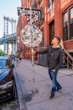 New York, ABD. 10 Mayıs 2019. Washington caddesinde yürüyen genç adam, Brooklyn 'de arka planda bir Manhattan köprüsü ile.