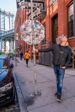 New York, ABD. 10 Mayıs 2019. Washington caddesinde yürüyen genç adam, Brooklyn 'de arka planda bir Manhattan köprüsü ile.