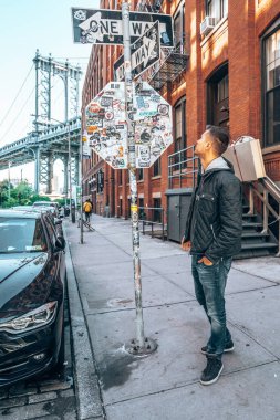 New York, ABD. 10 Mayıs 2019. Washington caddesinde yürüyen genç adam, Brooklyn 'de arka planda bir Manhattan köprüsü ile.