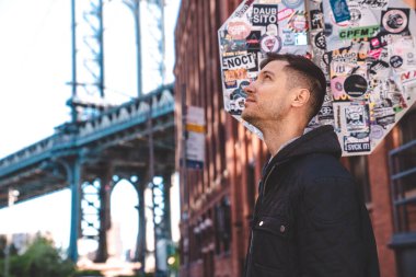 New York, ABD. 10 Mayıs 2019. Washington caddesinde yürüyen genç adam, Brooklyn 'de arka planda bir Manhattan köprüsü ile.