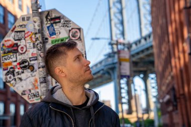 New York, ABD. 10 Mayıs 2019. Washington caddesinde yürüyen genç adam, Brooklyn 'de arka planda bir Manhattan köprüsü ile.