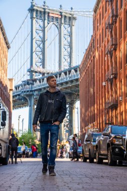 Washington caddesinde yürüyen genç adam, Brooklyn 'de arka planda bir Manhattan köprüsü ile.