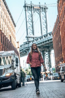 New York, ABD. 10 Mayıs 2019. Washington caddesinde yürüyen genç ve güzel bir bayan, Brooklyn 'de arka planda bir Manhattan köprüsü ile.