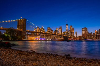 Brooklyn Köprüsü 'nün, Brooklyn Parkı' ndan Hudson Nehri 'nin diğer tarafındaki Manhattan manzaralı büyülü akşam günbatımı manzarası..