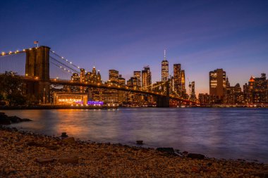 Brooklyn Köprüsü 'nün, Brooklyn Parkı' ndan Hudson Nehri 'nin diğer tarafındaki Manhattan manzaralı büyülü akşam günbatımı manzarası..