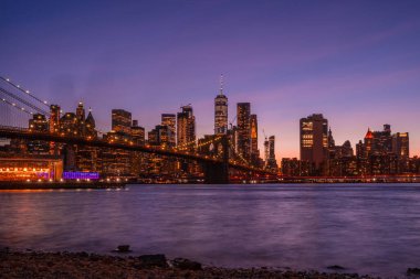 Brooklyn Parkı 'ndan Brooklyn Köprüsü' nün büyülü akşam mor gün batımı manzarası Hudson Nehri 'nin diğer tarafındaki Manhattan manzaralı..