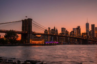 Brooklyn Köprüsü 'nün, Brooklyn Parkı' ndan Hudson Nehri 'nin diğer tarafındaki Manhattan manzaralı büyülü akşam günbatımı manzarası..