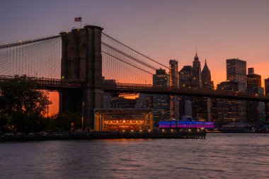 Brooklyn Köprüsü 'nün, Brooklyn Parkı' ndan Hudson Nehri 'nin diğer tarafındaki Manhattan manzaralı büyülü akşam günbatımı manzarası..