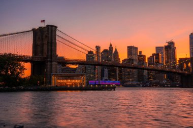 Brooklyn Köprüsü 'nün, Brooklyn Parkı' ndan Hudson Nehri 'nin diğer tarafındaki Manhattan manzaralı büyülü akşam günbatımı manzarası..