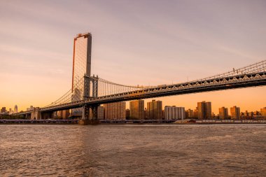 Manhattan Köprüsü 'nün Brooklyn Parkı' ndan Hudson Nehri 'nin diğer tarafındaki Manhattan manzaralı büyülü akşam günbatımı manzarası..