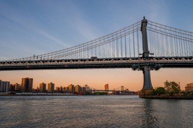 Manhattan Köprüsü 'nün Brooklyn Parkı' ndan Hudson Nehri 'nin diğer tarafındaki Manhattan manzaralı büyülü akşam günbatımı manzarası..