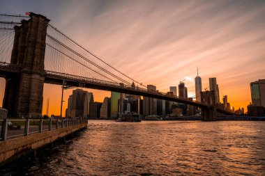 Brooklyn Köprüsü 'nün, Brooklyn Parkı' ndan Hudson Nehri 'nin diğer tarafındaki Manhattan manzaralı büyülü akşam günbatımı manzarası..
