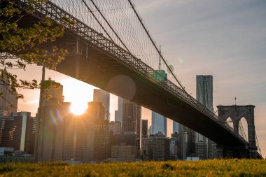 Brooklyn Köprüsü 'nün, Brooklyn Parkı' ndan Hudson Nehri 'nin diğer tarafındaki Manhattan manzaralı büyülü akşam günbatımı manzarası..