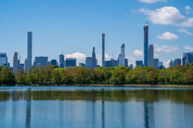 New York 'taki Central Park' ta güneşli bir günde göletin kenarında gökdelenlerle çevrili.