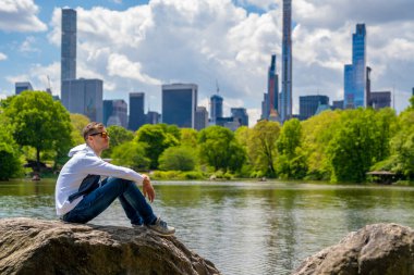 New York 'ta Central Park' ı keşfeden yakışıklı bir adam. Güneşli bir günde, göletin kenarında. Etrafı gökdelenlerle çevrili.