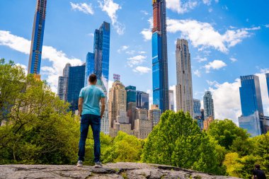 New York 'ta Central Park' ı keşfeden genç adam güneşli bir günde gökdelenlerle çevrili ana gölette.