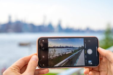 New York, ABD. 10 Mayıs 2019. Williamsburg, New York 'taki Domino Park tabelasından Manhattan manzarasının fotoğrafını çeken bir kız..