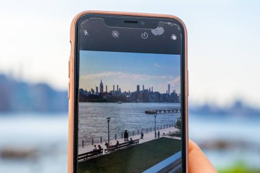 New York, ABD. 10 Mayıs 2019. Williamsburg, New York 'taki Domino Park tabelasından Manhattan manzarasının fotoğrafını çeken bir kız..