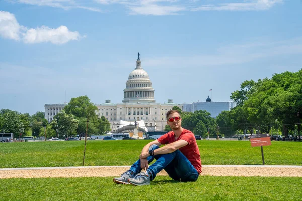 Young man sitting on the grass by the United States Capitol in Washington, DC.