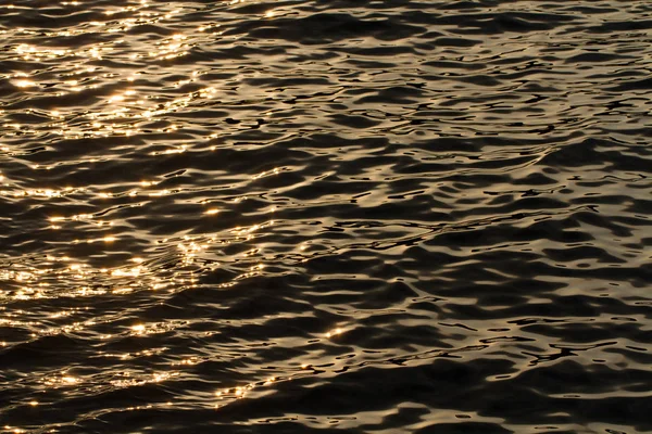 The surface of the ocean at sunset with the golden glow of the sun reflected on the ripples.