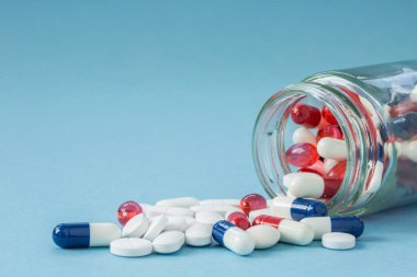 A medicine concept of an upturned jar full of medicines, drugs, tablets and pills spilling out onto a blue background with copy space. clipart